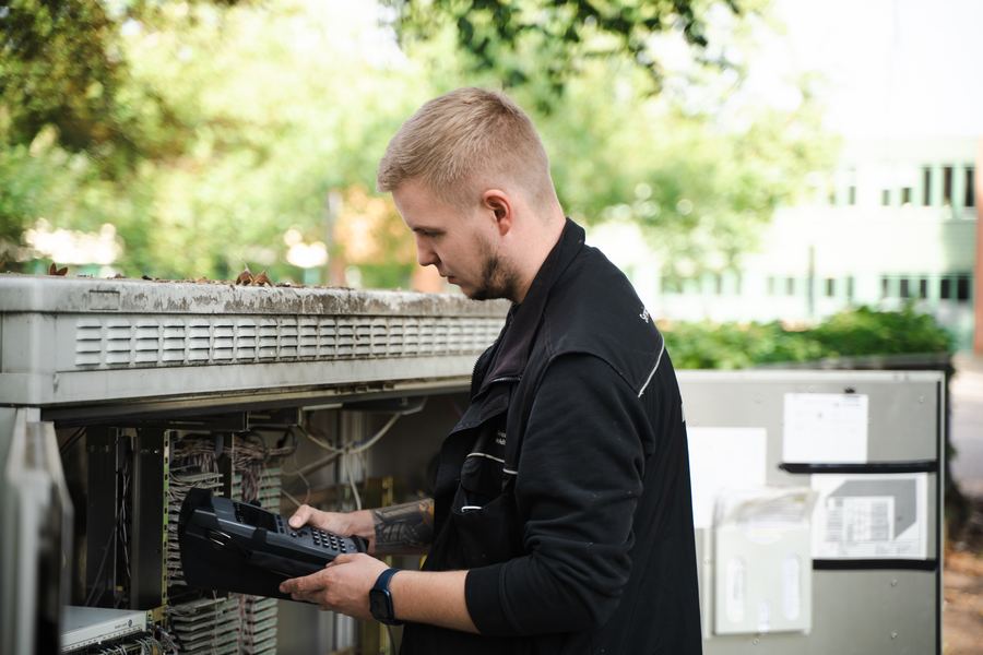 Junger Techniker mit ASA-Servicehandapparat vor geöffnetem Outdoor-KVz